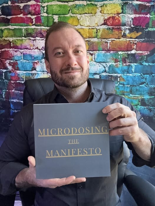 Coach smiling and holding the book titled Microdosing the Manifesto
